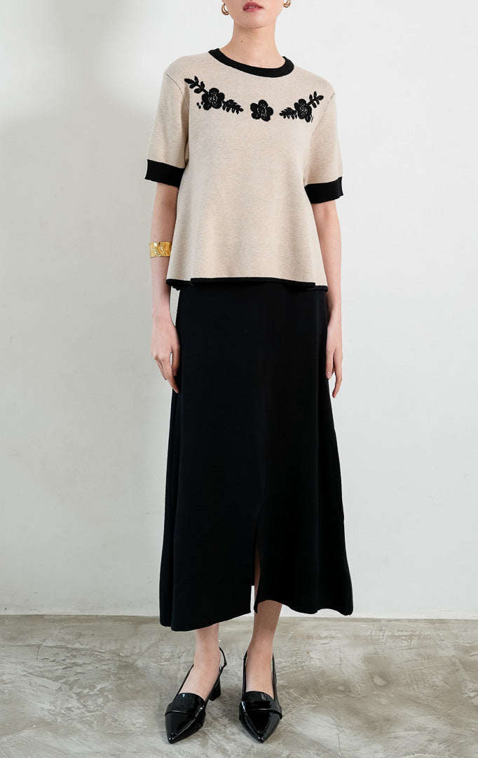 Atasan rajut wanita lengan pendek warna khaki Coreen Top berpotongan peplum dengan kerah bulat lis hitam kontras (black ribbed trim), serta aksen bordir bunga hitam di bagian dada (black floral embroidery).