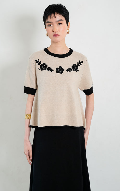 Atasan rajut wanita lengan pendek warna khaki Coreen Top berpotongan peplum dengan kerah bulat lis hitam kontras (black ribbed trim), serta aksen bordir bunga hitam di bagian dada (black floral embroidery).