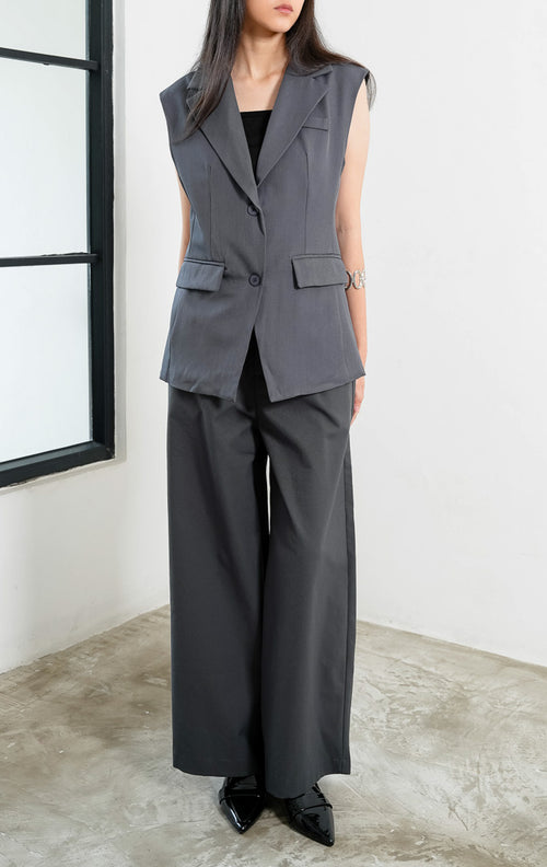 Rompi blazer wanita terstruktur warna abu-abu (grey tailored vest) Crawford Vest dengan detail kerah lebar (wide notched lapel), bukaan dua kancing depan (double-button front closure), panel tegas, dan saku penutup di bagian pinggang (flap pockets). 