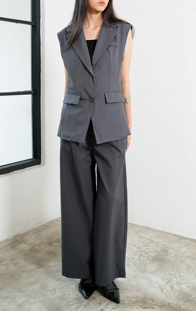 Rompi blazer wanita terstruktur warna abu-abu (grey tailored vest) Crawford Vest dengan detail kerah lebar (wide notched lapel), bukaan dua kancing depan (double-button front closure), panel tegas, dan saku penutup di bagian pinggang (flap pockets). 