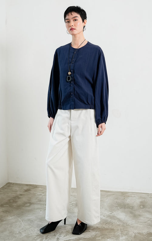Blus wanita bahan katun ringan warna biru dongker (navy) Damian Top dengan kerah bulat (round neckline), bukaan kancing depan, lengan panjang bervolume manset karet (voluminous sleeves with elasticated cuffs), dan bagian bawah berkerut karet (elastic hem).