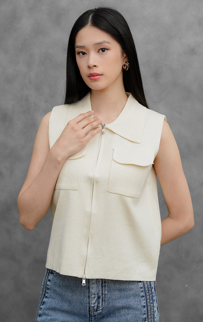 Rompi rajut (knit vest) wanita tanpa lengan warna krem muda (ivory) Danielle Vest dengan kerah lancip (pointed collar), bukaan resleting depan (front zip closure), dan dua saku tempel fungsional di dada.
