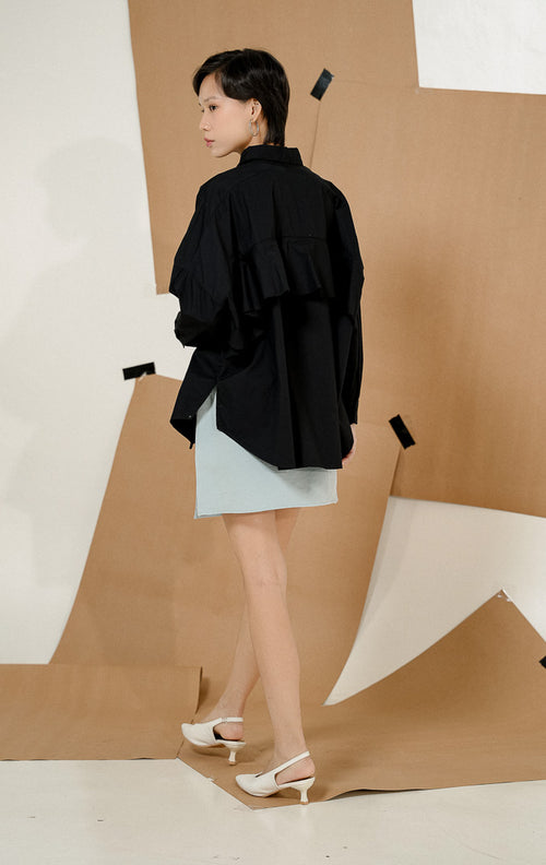 Model tampak belakang mengenakan Dayle Top Black, produk kemeja kerja kantor wanita lengan panjang warna hitam dengan detail ruffle unik di bagian punggung. 