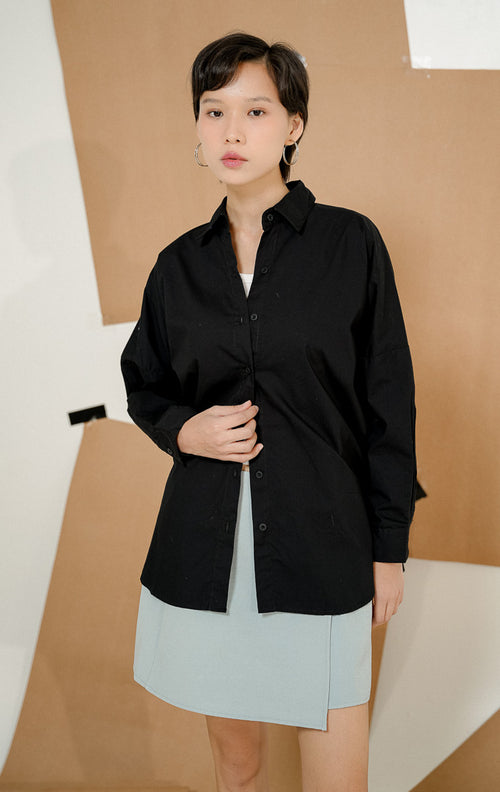 Model tampak belakang mengenakan Dayle Top Black, produk kemeja kerja kantor wanita lengan panjang warna hitam dengan detail ruffle unik di bagian punggung. 