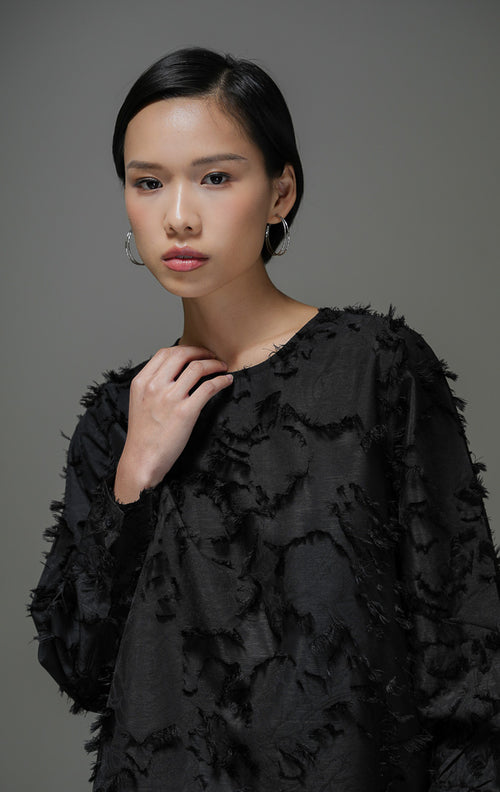 Blouse wanita Demetrius Top warna hitam lengan panjang dengan tekstur bulu halus (fringe jacquard), kerah bulat, dan kancing belakang.