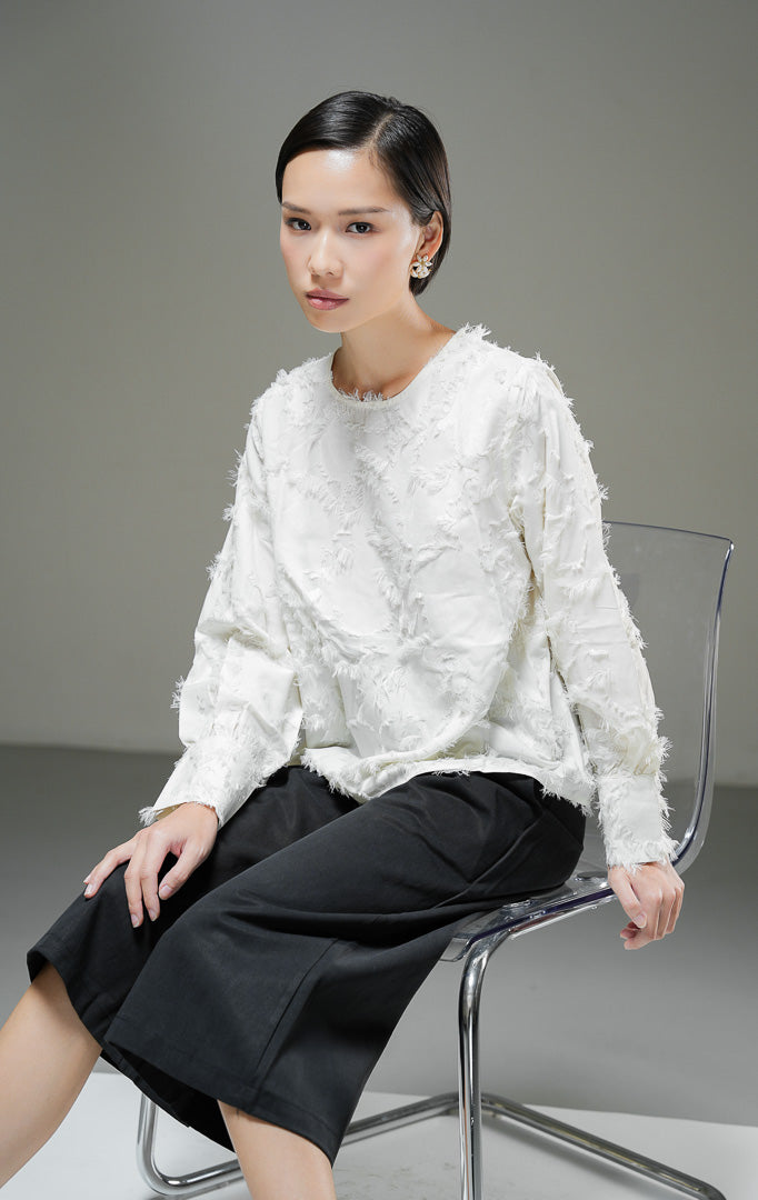 Blouse wanita Demetrius Top warna ivory krem muda lengan panjang dengan tekstur bulu halus (fringe jacquard), kerah bulat, dan kancing belakang. 