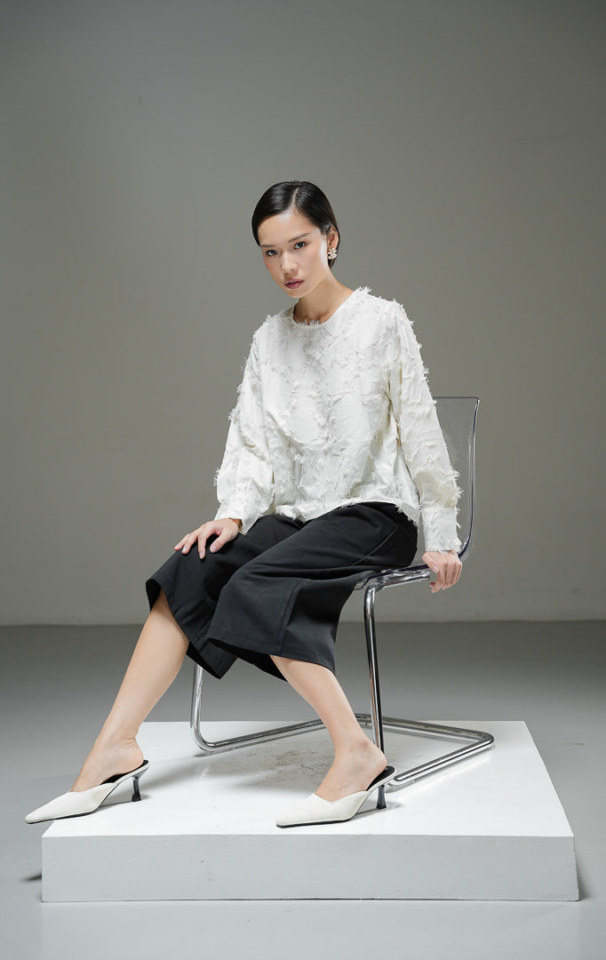 Blouse wanita Demetrius Top warna ivory krem muda lengan panjang dengan tekstur bulu halus (fringe jacquard), kerah bulat, dan kancing belakang. 