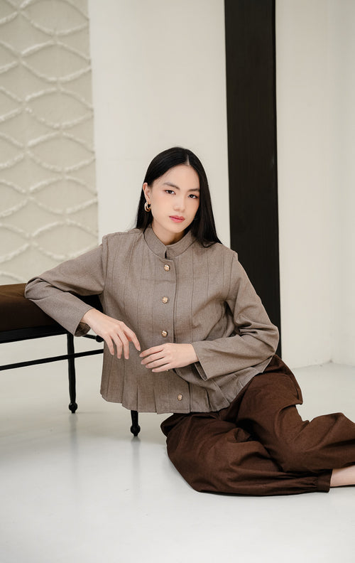 Outerwear wanita tanpa kerah (round-neck) Denali warna brown (cokelat) bertekstur lipit vertikal (pleated) dengan detail kancing emas (gold buttons) tampak depan.