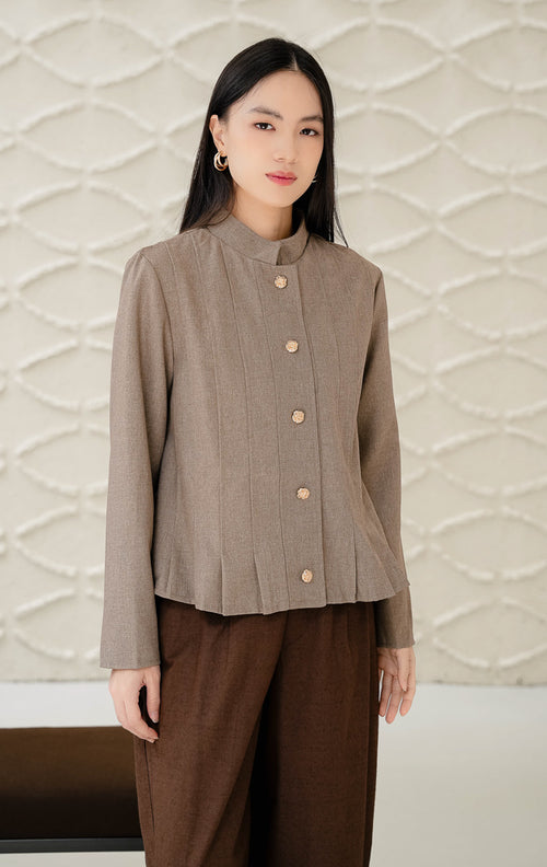Outerwear wanita tanpa kerah (round-neck) Denali warna brown (cokelat) bertekstur lipit vertikal (pleated) dengan detail kancing emas (gold buttons) tampak depan.