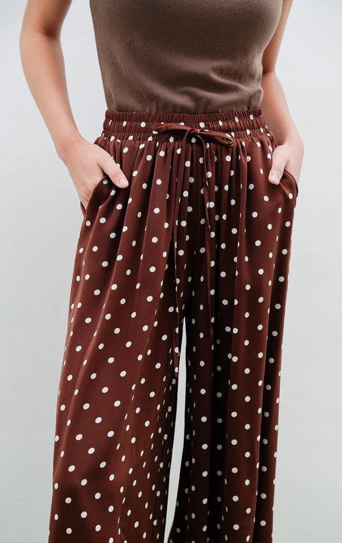 Celana panjang wanita warna cokelat tua (dark brown) Dotsie Pants berbahan satin halus motif polkadot dengan potongan relaxed fit dan saku samping.