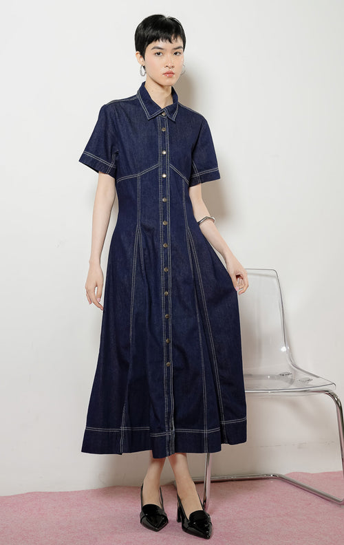 Model wanita mengenakan Lumera Classic Flared Maxi Dress warna dark denim, gaun dress panjang bahan jeans wanita lengan pendek berwarna biru dongker dengan detail jahitan kontras putih. 
