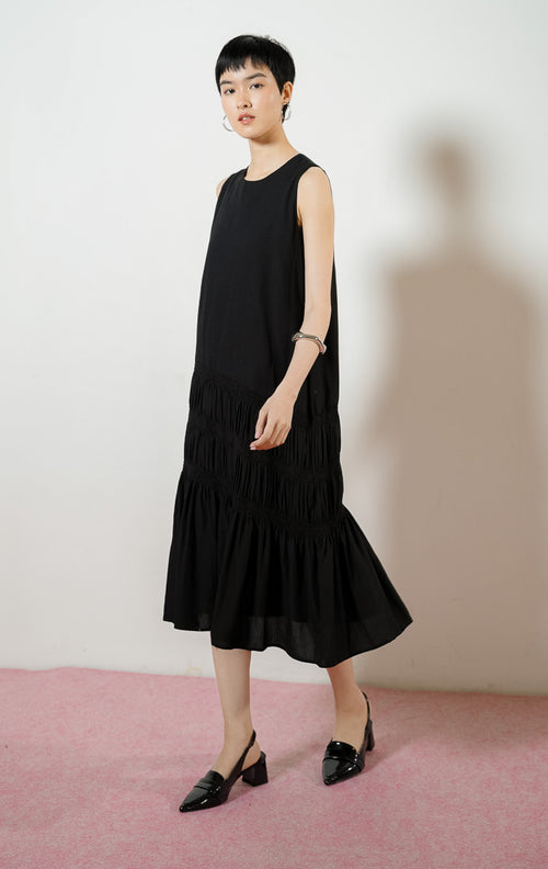 Model wanita mengenakan Ravena Shirred Bodice Drop-Tier Maxi Dress warna black, gaun panjang dress tanpa lengan wanita warna hitam dengan detail aksen serut karet smok bertingkat di rok. 