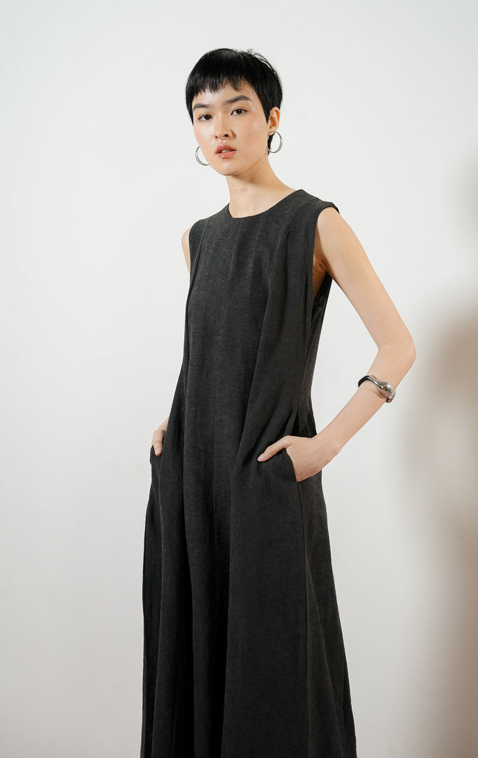 Model wanita mengenakan Abrielle Dress warna black, midi dress tanpa lengan wanita berwarna hitam dengan detail lipit bahu dan saku samping fungsional.