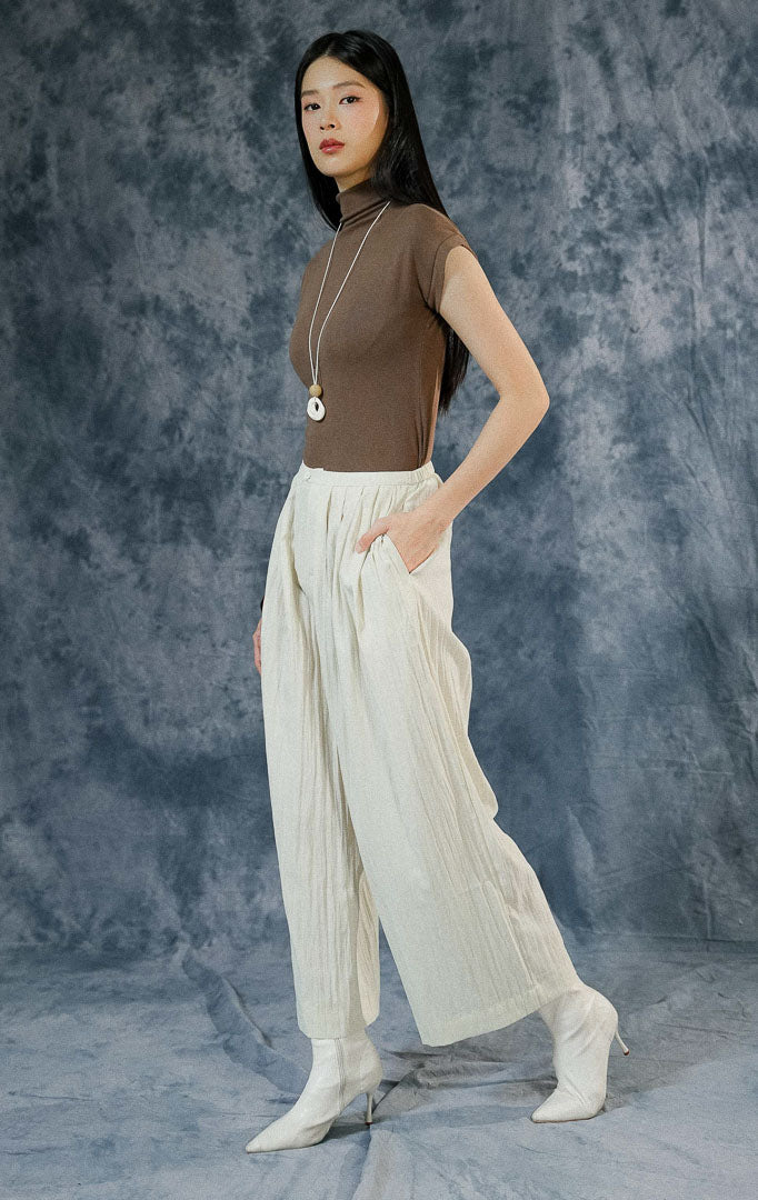 Celana panjang wanita Echo warna ivory dengan cutting loose pants kulot, berbahan crinkle-polyester flowy, dilengkapi saku samping dan resleting depan.