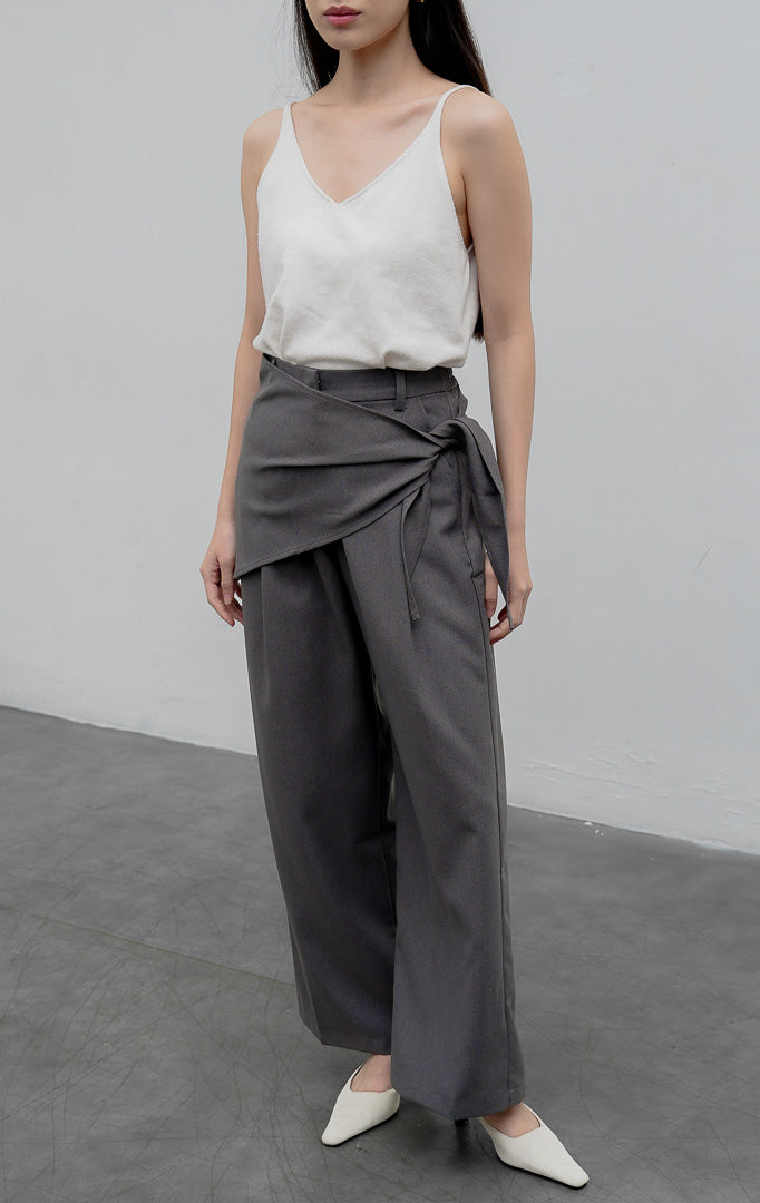 Celana kulot wanita model longgar (wide-leg pants) warna abu-abu (grey) Edliana Pants berbahan cotton-polyester dengan detail lapisan silang (overlap wrap), sabuk tali asimetris (asymmetrical belt), dan karet pinggang belakang.