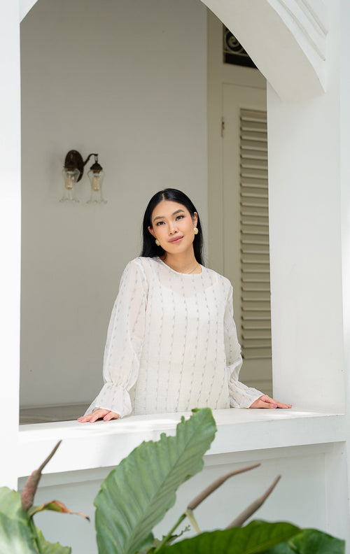 Model mengenakan EID Aniza Top Grey, atasan wanita bahan cotton 
organza warna abu abu transparan dengan motif bordir bunga vertikal dan 
ujung lengan model flare