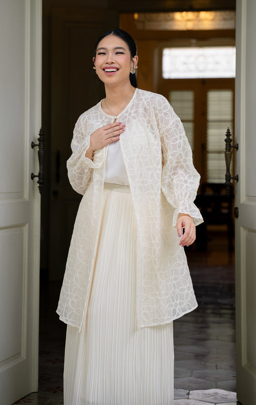 EID Fariha Top Ivory, atasan wanita warna putih gading bahan cotton voile 
transparan dengan motif bordir bunga lingkaran penuh, kancing tunggal di 
leher, dan ujung lengan model flare kerut.