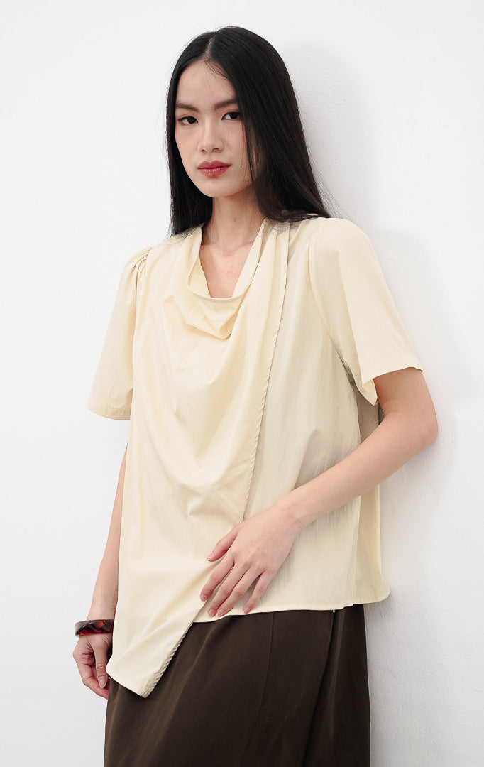 Close up model mengenakan Eileen Top warna yellow, menampilkan detail kerah draped cowl neck yang elegan dan kancing dekoratif di bahu.