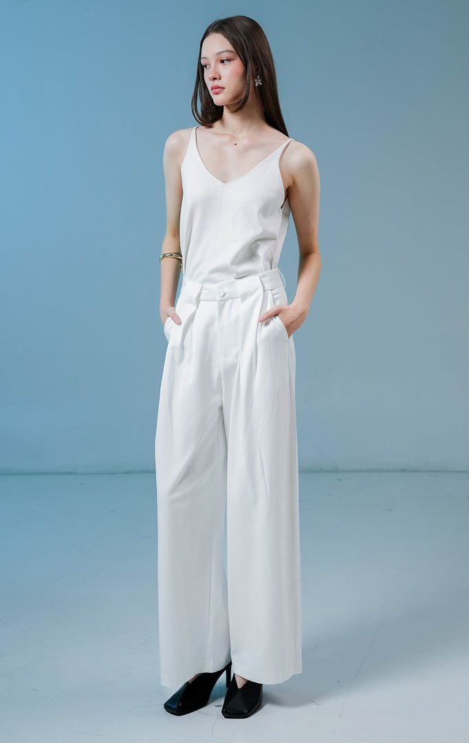 Model wanita mengenakan Normandy Pleated Straight Pants warna white, celana panjang bahan katun wanita berwarna putih dengan detail lipit depan dan potongan straight-leg. 