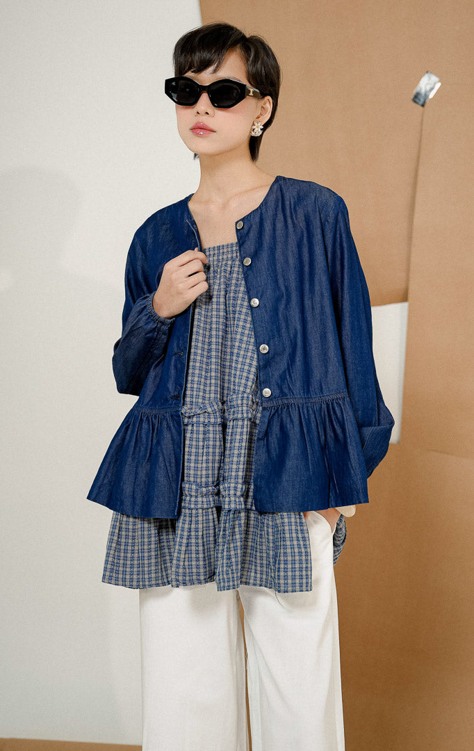 Model mengenakan kacamata hitam dan Deliana Round-Neck Ruffle Hem Denim Top Indigo, produk atasan denim wanita warna biru indigo dengan kancing depan dan detail rempel.