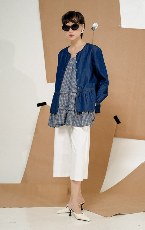 Model mengenakan kacamata hitam dan Deliana Round-Neck Ruffle Hem Denim Top Indigo, produk atasan denim wanita warna biru indigo dengan kancing depan dan detail rempel.