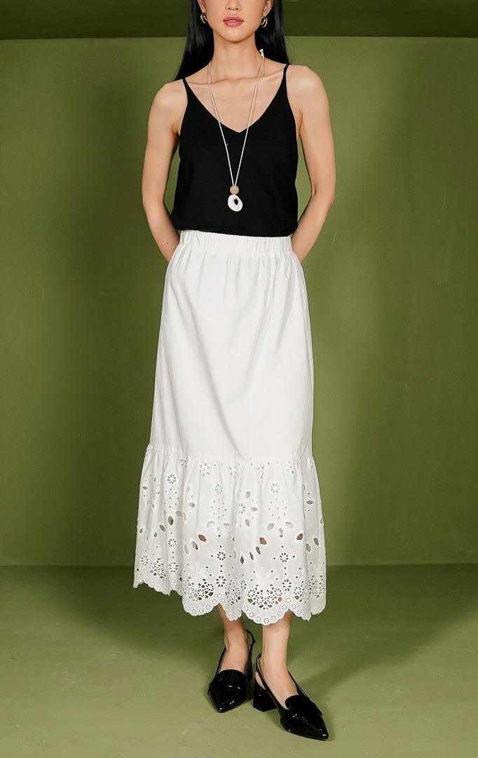 Rok wanita Eliana Skirt berwarna putih dengan pinggang karet elastis, bagian atas katun polos, dan bagian bawah dihiasi detail bordir crochet berlubang serta ujung bergelombang (scallop hem).