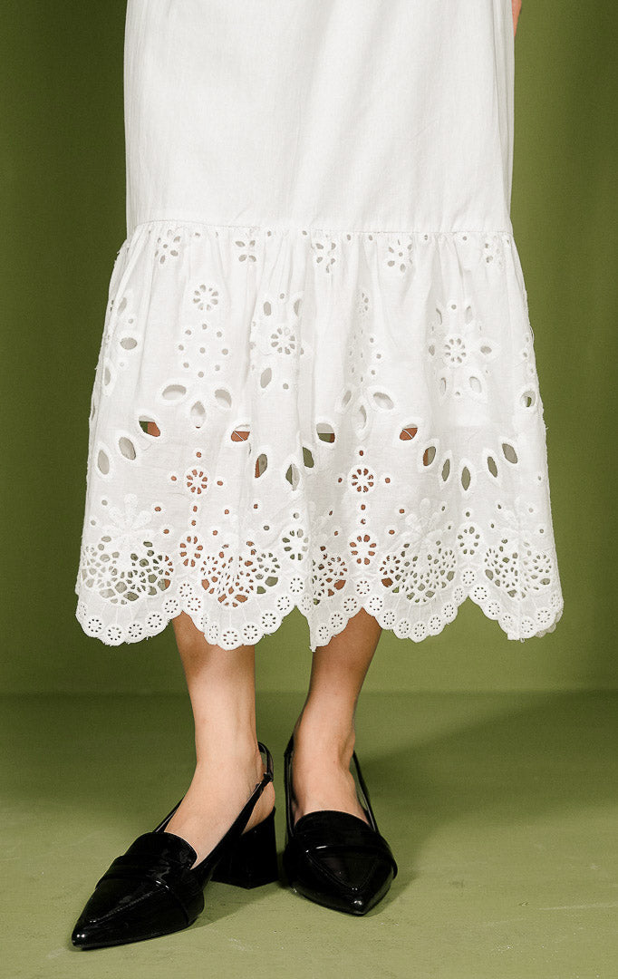 Rok wanita Eliana Skirt berwarna putih dengan pinggang karet elastis, bagian atas katun polos, dan bagian bawah dihiasi detail bordir crochet berlubang serta ujung bergelombang (scallop hem).