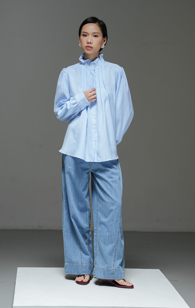 Kemeja wanita Ellenore Top warna biru motif garis salur (stripe) lengan panjang dengan detail kerah ruffle rumbai manis dan kancing depan. 