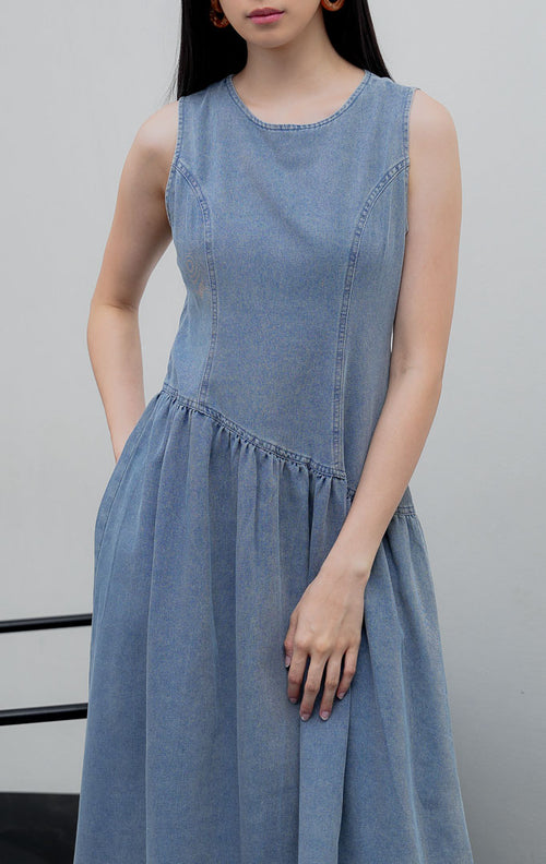 Gaun terusan tanpa lengan (sleeveless dress) wanita warna biru muda denim (light denim) Elodie Dress berpotongan A-line dengan detail potongan bawah asimetris (asymmetric hem) dan resleting belakang.