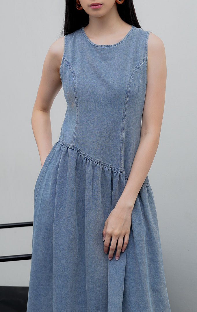 Gaun terusan tanpa lengan (sleeveless dress) wanita warna biru muda denim (light denim) Elodie Dress berpotongan A-line dengan detail potongan bawah asimetris (asymmetric hem) dan resleting belakang.