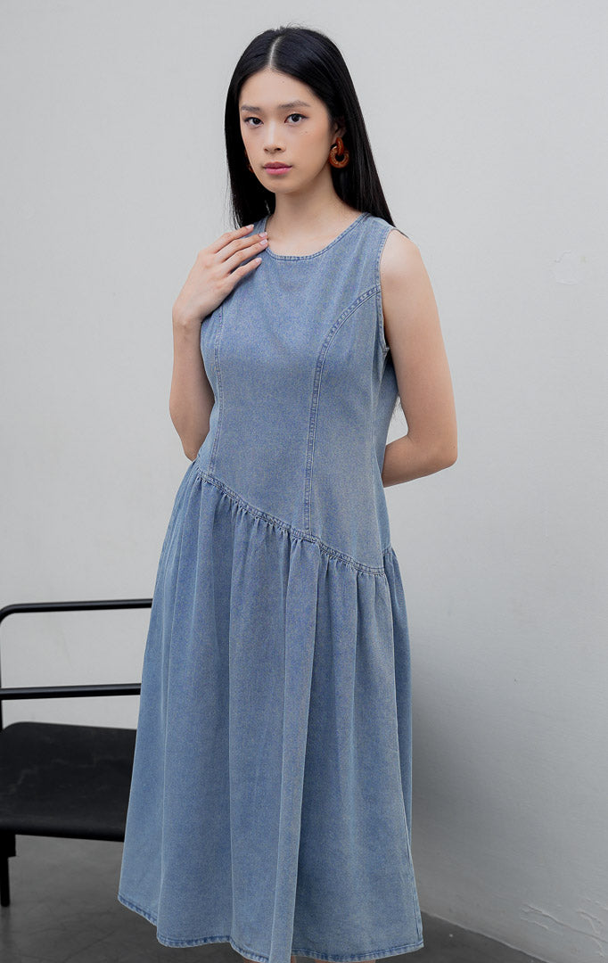 Gaun terusan tanpa lengan (sleeveless dress) wanita warna biru muda denim (light denim) Elodie Dress berpotongan A-line dengan detail potongan bawah asimetris (asymmetric hem) dan resleting belakang.