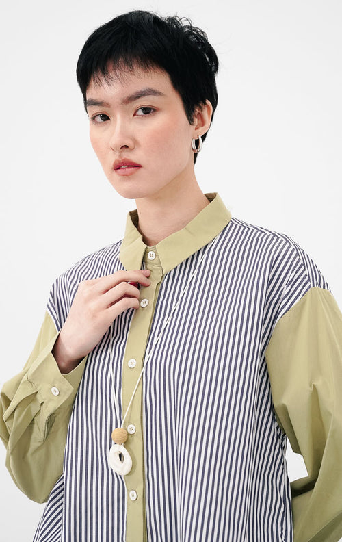 Close up model mengenakan Emerald Top warna sage, menampilkan detail kemeja motif garis vertikal biru putih dengan kerah dan bagian kancing berwarna sage green.