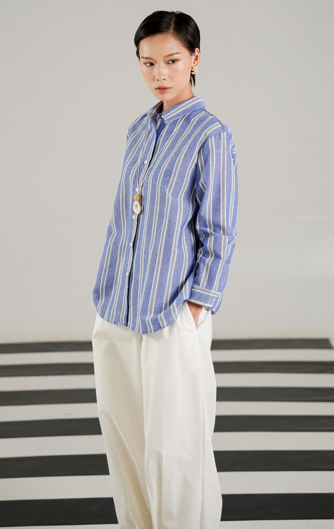 Kemeja lengan panjang wanita Ericka Top Blue dengan motif garis garis vertikal biru putih, detail kerah rapi, dan kancing depan dari This Is April.
