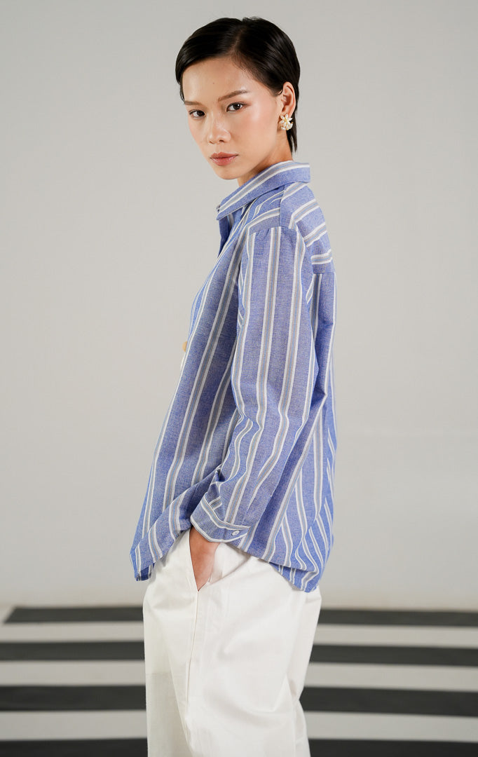 Kemeja lengan panjang wanita Ericka Top Blue dengan motif garis garis vertikal biru putih, detail kerah rapi, dan kancing depan dari This Is April.
