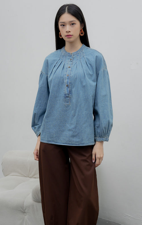 Atasan denim chambray wanita lengan panjang warna biru medium (denim) Eriu Top berbahan non-stretch dengan aksen lipit (pleated design) dan bukaan kancing setengah (half-placket)