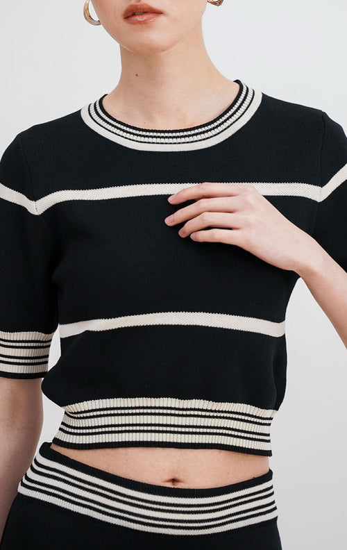 Model mengenakan Esmeralda Knit Set warna black, setelan rajut motif garis putih horizontal terdiri dari atasan crop lengan pendek dan rok midi high-waist