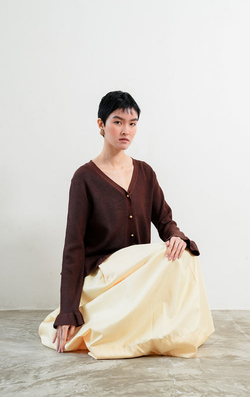 Kardigan rajut wanita lengan panjang warna cokelat tua (dark brown) Eugenia Cardigan berstruktur knit dengan potongan pinggang mekar (peplum silhouette), leher V (V-neckline), dan kancing emas (gold-tone buttons). 