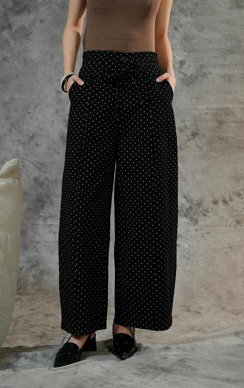 Celana panjang wanita Evelyna warna hitam bermotif polkadot dengan cutting barrel pants, berbahan denim, dilengkapi karet pinggang belakang dan aksen tali pita.