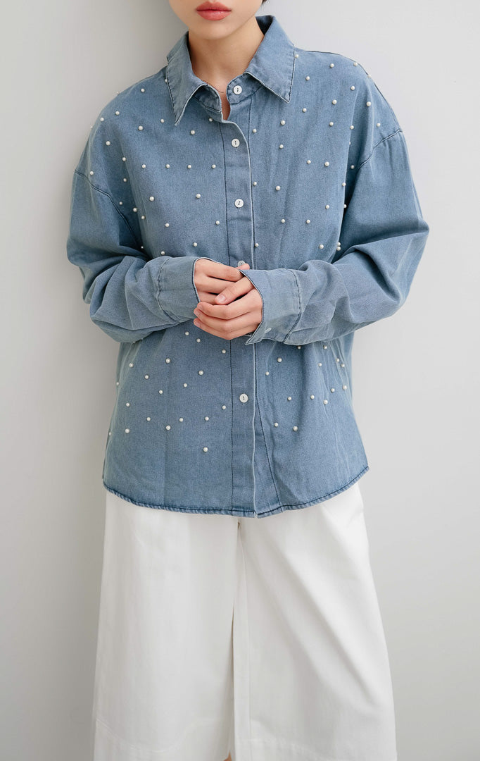 Atasan kemeja denim wanita lengan panjang Faye Top dengan detail hiasan mutiara (pearl details), bukaan kancing depan, dan siluet berstruktur.