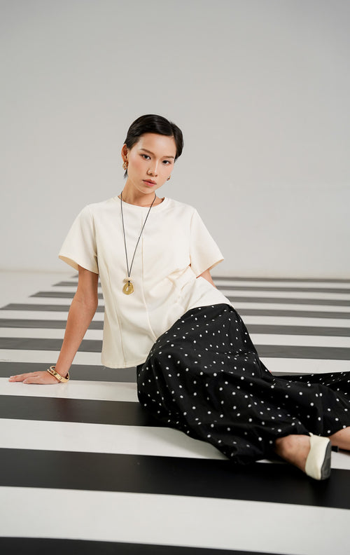 Atasan wanita Fernandez Top warna Ivory dengan detail jahitan vertikal terstruktur di bagian depan, kerah bulat, dan lengan pendek dari This Is April. 
