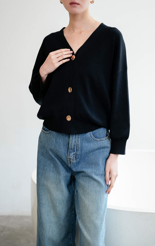 Luaran rajut wanita (knit outer) lengan panjang warna hitam (black) Fletcher Outer berbahan rajut elastis (stretchable knit) dengan leher V (V-neck) dan bukaan kancing emas (gold buttons).