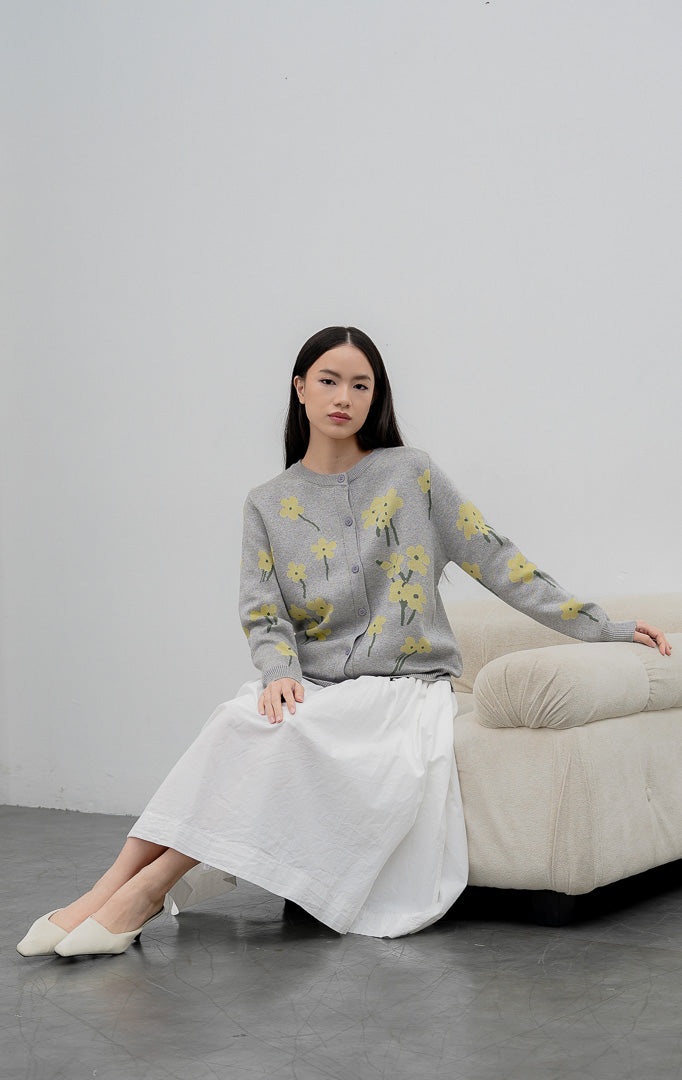 Sweter rajut wanita lengan panjang warna abu-abu (grey) Fleur Sweater dengan motif bunga kuning (floral print), kerah bulat (crew neck), dan kancing depan.