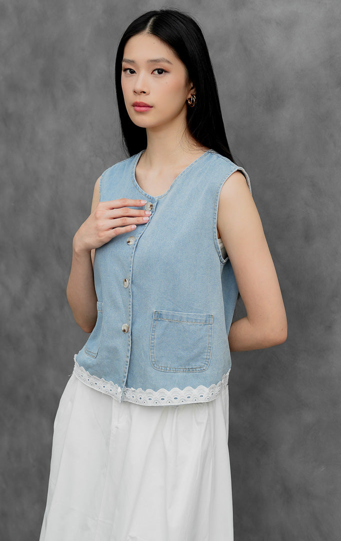Rompi jeans wanita tanpa lengan warna biru muda (light denim) Flossie Vest dengan aksen renda kelim (scallop eyelet lace detail), bukaan kancing depan, dan saku fungsional.