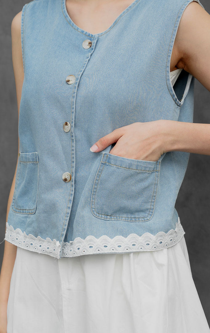 Rompi jeans wanita tanpa lengan warna biru muda (light denim) Flossie Vest dengan aksen renda kelim (scallop eyelet lace detail), bukaan kancing depan, dan saku fungsional.