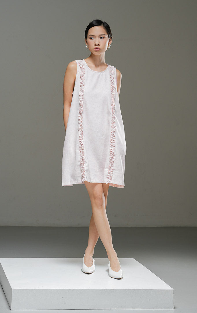Dress linen wanita tanpa lengan Francoise Dress warna pink merah muda lembut dengan aksen aksesoris ruffle vertikal di bagian depan dan kerah bulat. 