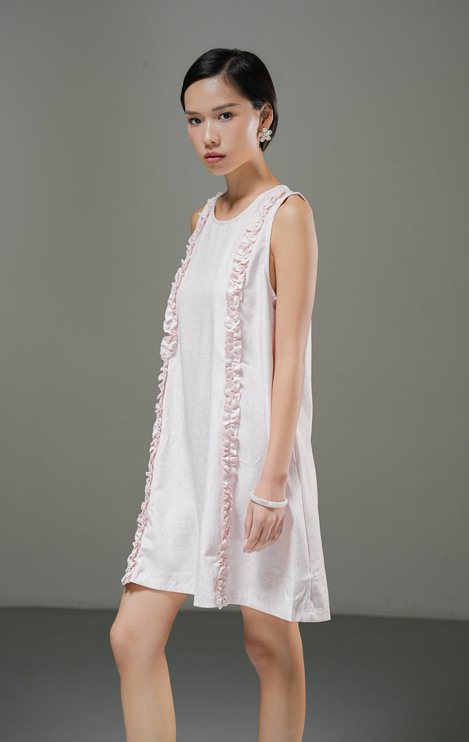 Dress linen wanita tanpa lengan Francoise Dress warna pink merah muda lembut dengan aksen aksesoris ruffle vertikal di bagian depan dan kerah bulat. 