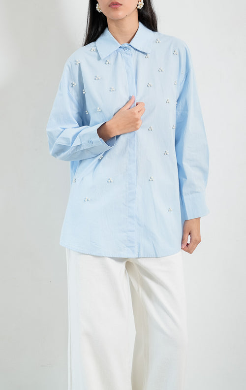 Kemeja wanita lengan panjang warna biru muda (light blue) Freesia Top dengan kerah klasik (classic collar), bukaan kancing depan tertutup, dan hiasan manik mutiara motif bunga (pearl bead embellishments). 