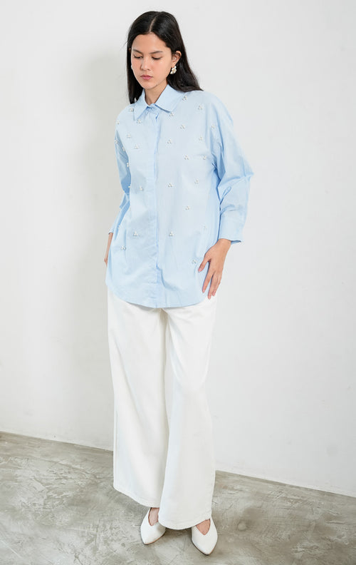 Kemeja wanita lengan panjang warna biru muda (light blue) Freesia Top dengan kerah klasik (classic collar), bukaan kancing depan tertutup, dan hiasan manik mutiara motif bunga (pearl bead embellishments). 