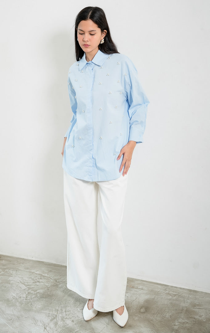 Kemeja wanita lengan panjang warna biru muda (light blue) Freesia Top dengan kerah klasik (classic collar), bukaan kancing depan tertutup, dan hiasan manik mutiara motif bunga (pearl bead embellishments). 