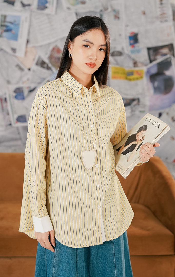 Model wanita memakai Fukui Top Yellow kemeja lengan panjang motif garis vertikal kuning putih bahan katun dengan kerah kemeja klasik dan potongan longgar.